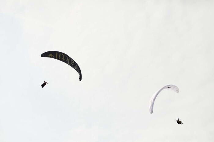 Zwei Paragleiter von hinten zu sehen und im Hintergrund ein wolkenreicher Himmel