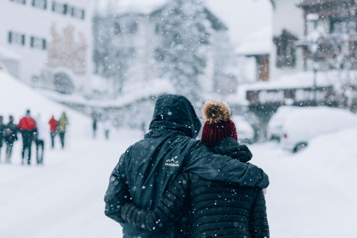 zwei Personen laufen Hand in Hand durch den Schnee im Dorfzentrum von Lech während es gerade schneit