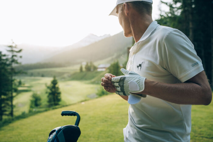 Golfer zieht sich den Golfhandschuh an für den nächsten Schlag und blickt in die Ferne