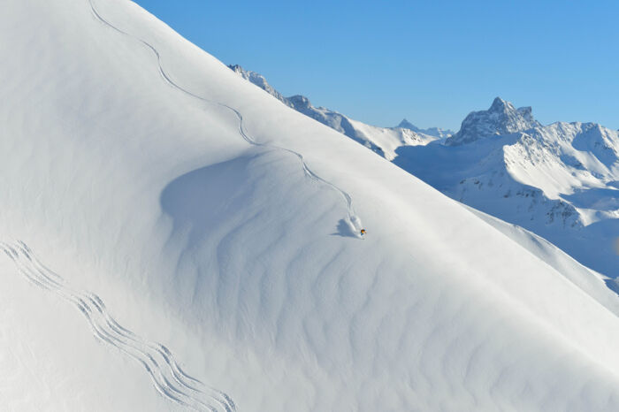 Skifahrer fährt einen offenen weiten weiß verschneiten Hang hinab und zieht die erste Line
