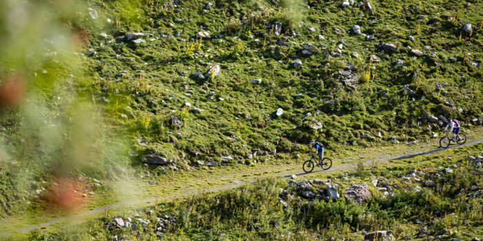 Zwei Radfahrer fahren durch eine grüne Wiese in den Bergen.