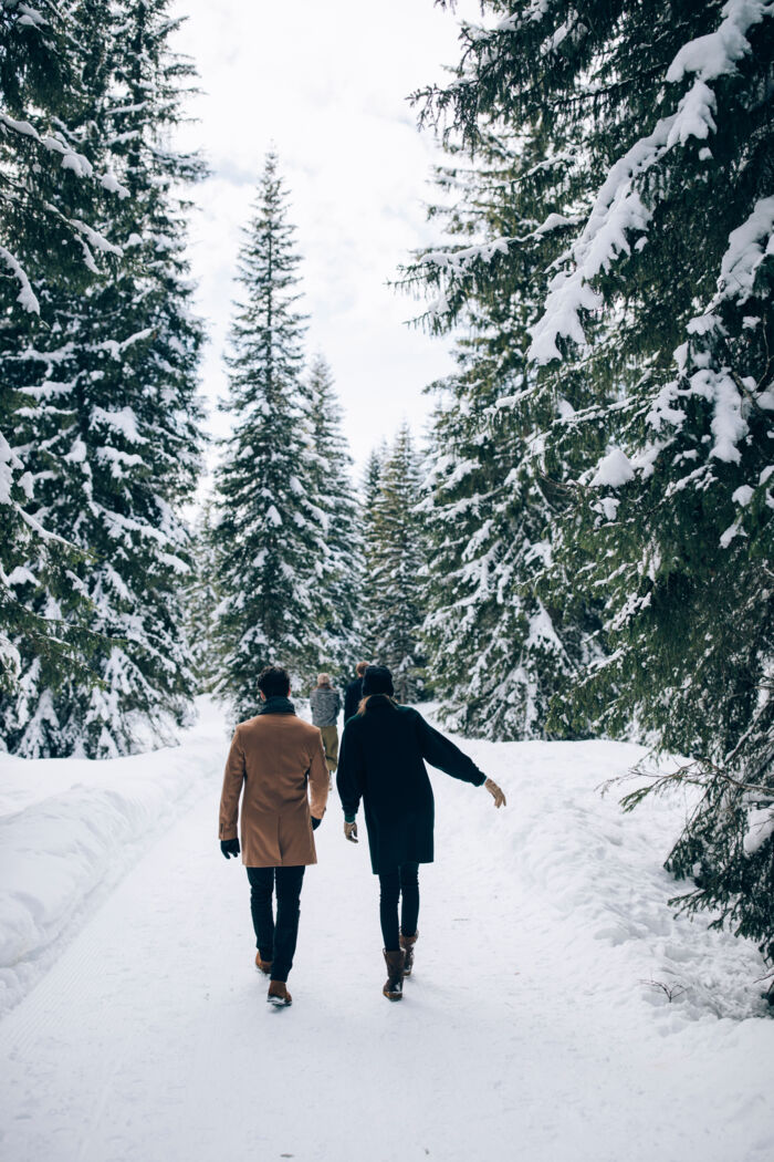 mehrere Personen laufen zwischen den schneebedeckten Nadelbäumen über den Winterwanderweg