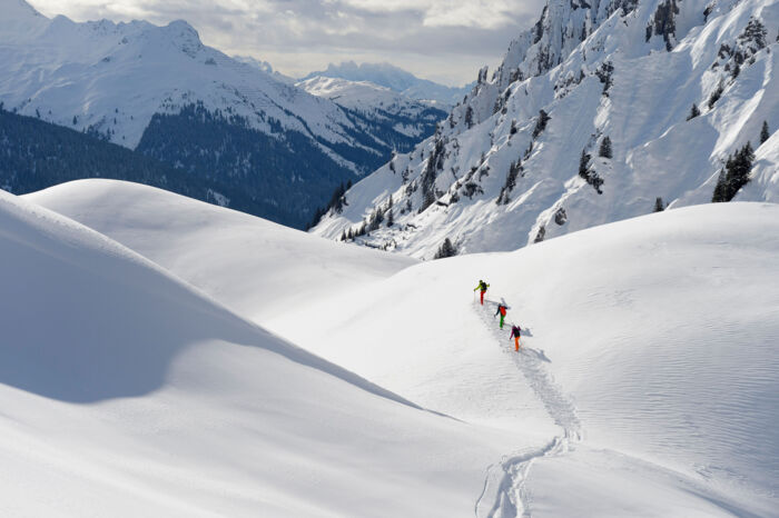 Drei Skifahrer stapfen im Gelände den Tiefschneehang hinauf für die nächste Abfahrt