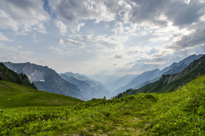 Das Sonnenlicht fällt durch die Wolkendecke, im Gebirge, satte gruene Wiesen und ein schoenes Bergpanorama