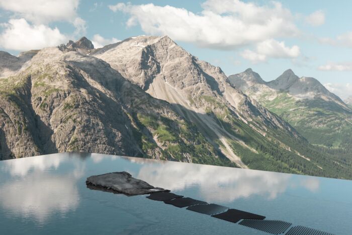Frau auf Felsen in einem spiegelnden Bergsee vor schroffem Alpenpanorama.