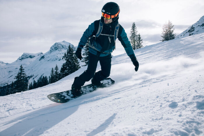 ein Snowboarder fährt über die frisch präparierte Piste bei traumhaftem Wetter, im Hintergrund sieht man das winterliche Bergpanorama