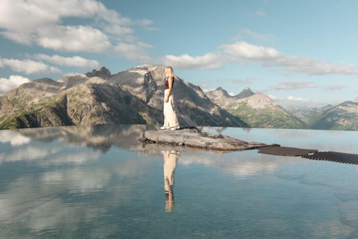 Frau auf Felsen in einem spiegelnden Bergsee vor schroffem Alpenpanorama.
