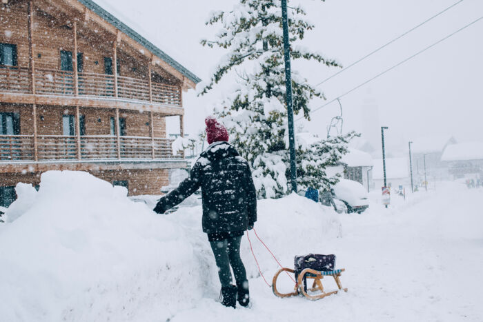 eine Person steht mit ihrem Rodel auf der schneebedeckten Straße während es gerade schneit