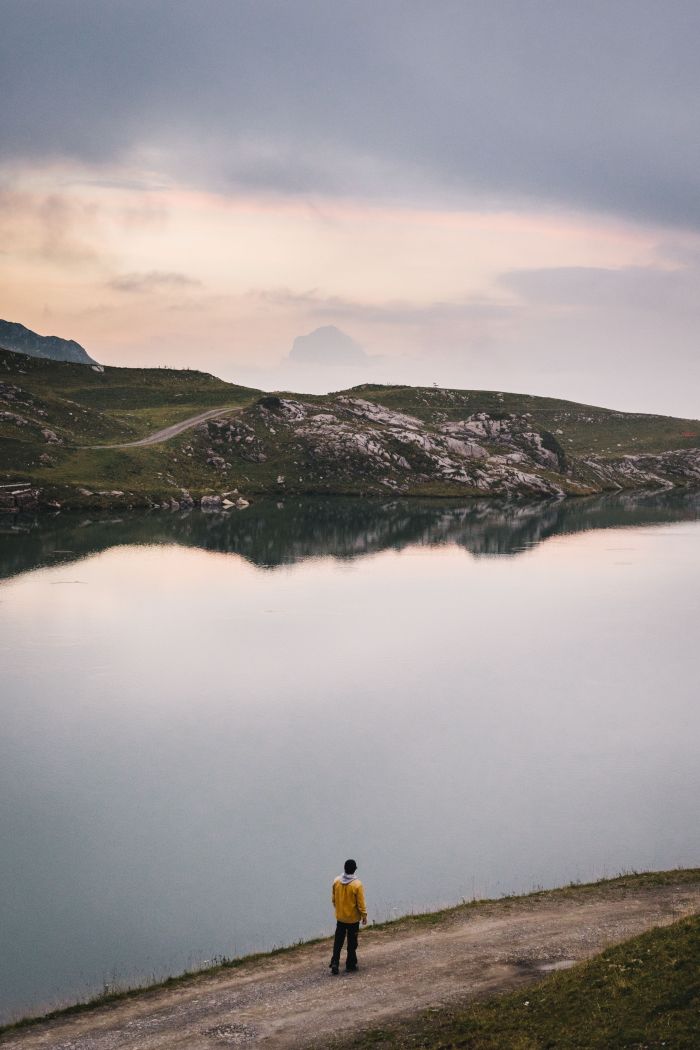 Wanderer steht am Ufer eines Bergsees und die Abenddämmerung spiegelt sich im Wasser