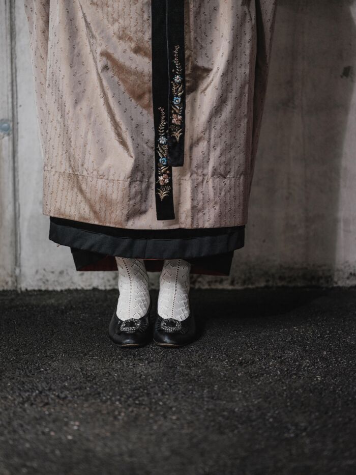 Traditioneller Walser Frauenrock in hellrosa und bestickten Baendern und weissen Socken