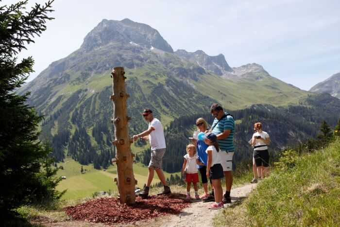 Eine Familie steht vor einer Station am Grünen Rätsel-Ring mit Omeshorn im Hintergrund