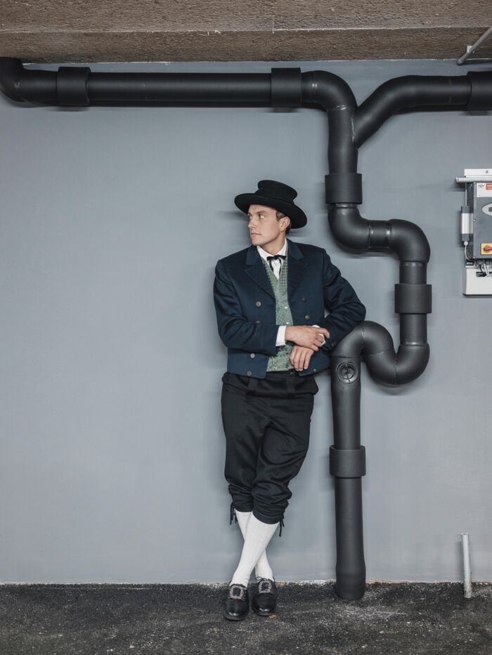 Mann in Walser Tracht mit schwarzen Hut, gruenes Gelee, blauer Blazer, Hose bis zu Knien und weißen Stutzen