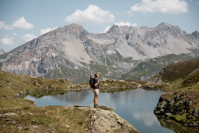 Wanderin mit Rucksack steht am Ufer des Unteren Maroisees und blickt auf die schroffe Bergkette dahinter.