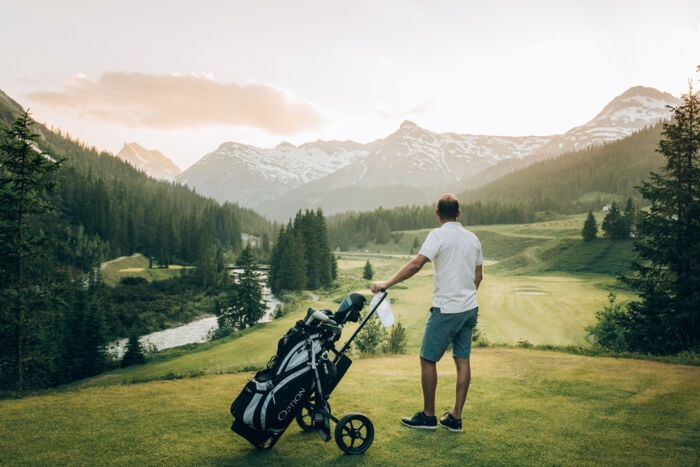 Golfer am Zuger Golfplatz sieht in die Ferne; im Hintergrund erstreckt sich der Lech sowie leicht angeschneite Berggipfel