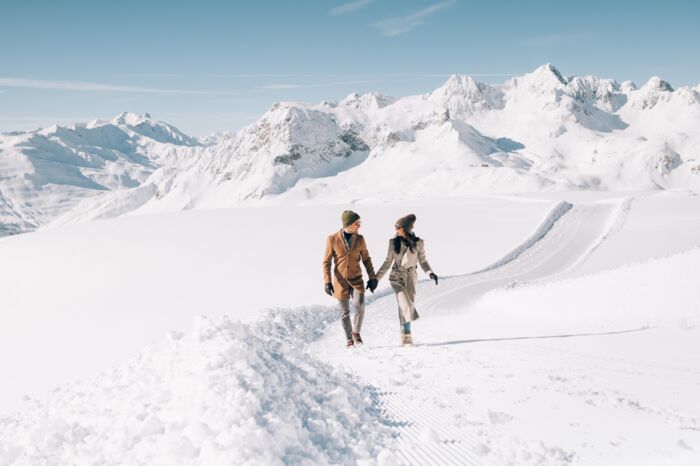 zwei Personen gehen über den Schneeflockenpanoramaweg am Rüfikopf bei Sonnenschein