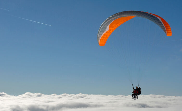 Zwei Tandemflieger im Gleitschirm über der Wolkendecke und strahlend blauen Himmel