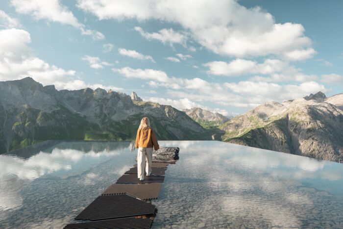 Frau auf Felsen in einem spiegelnden Bergsee vor schroffem Alpenpanorama.