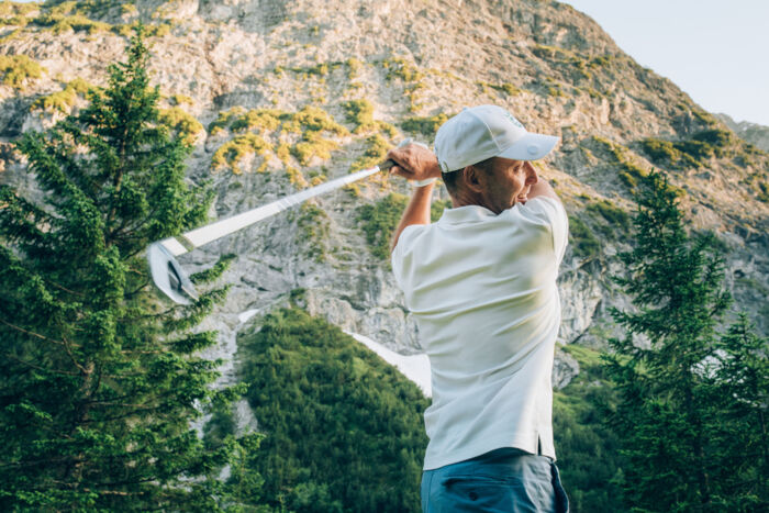 Golfer schwingt den Golfschläger am Zuger Golfplatz mit felsigem Berg im Hintergrund