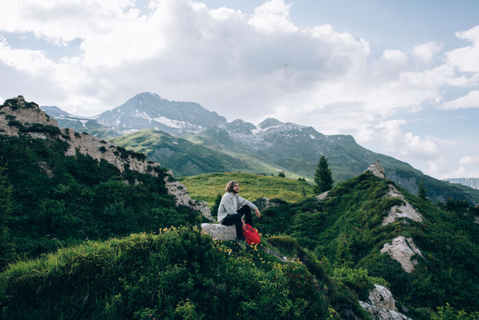 ein Wanderer macht eine Pause und genießt das traumhafte Bergpanorama inmitten von saftig grünen Wiesen