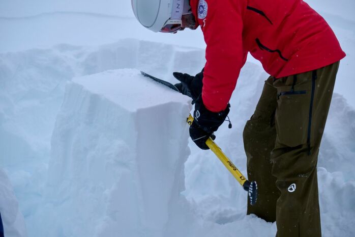 ein Mann in Skiausrüstung macht eine Schneedeckenprofilanalyse