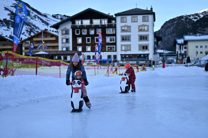 zwei Kinder fahren mit einer Eislaufhilfe Schlittschuhe auf dem Eislaufplatz in Zürs