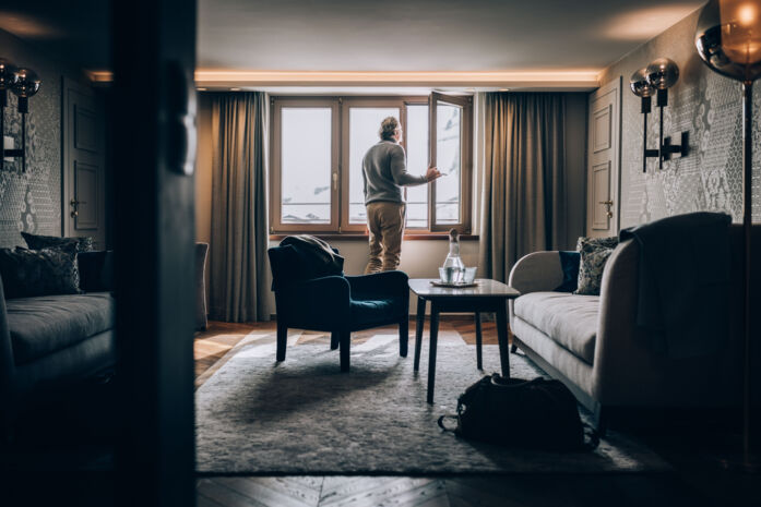 eine Person schaut aus dem Fenster eines Hotelzimmers hinaus