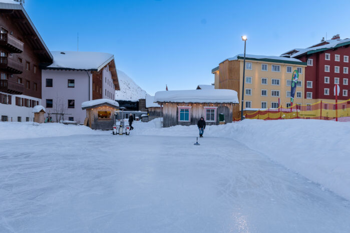 Blick auf den Eislaufplatz in Zürs mit dem winterlichen Ortsbild im Hintergrund