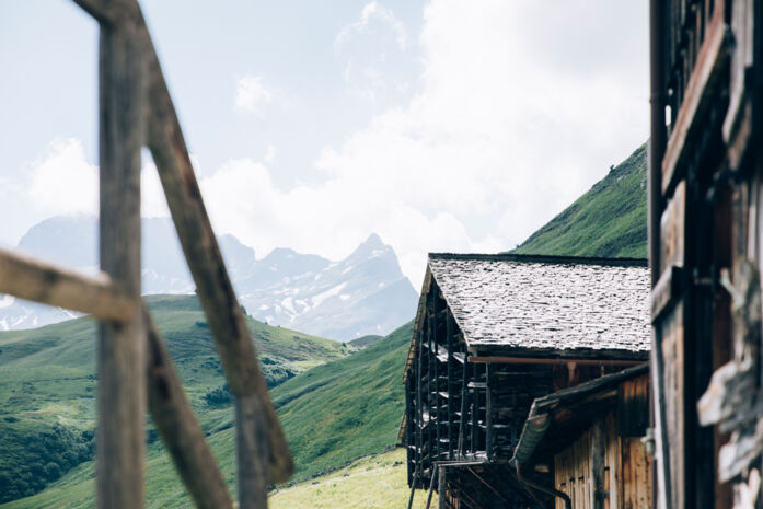 Blick von einer Terrasse auf ein anderes uriges Holzhaus in Bürstegg, im Hintergrund sieht man das Bergpanorama