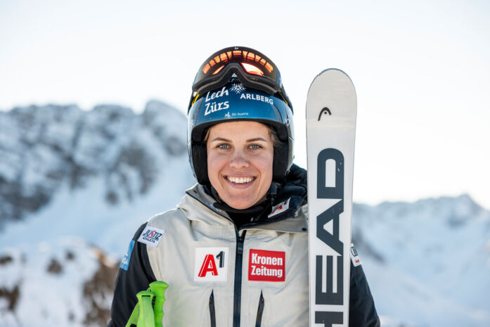Eine lachende Person Magdalena Egger im Bild mit Skihelm am Kopf und Lech Zürs Logo auf der Vorderseite zu sehen. Sie hält die HEAD Ski in den Händen