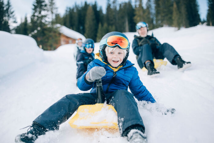 eine Familie rodelt voller Freude mit dem Zipfelbob über die Rodelbahn in Lech Zürs