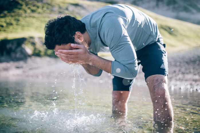 Wanderer steht bis zu den Knien im klaren Wasser des Butzensees und wäscht sich zur Erfrischung das Gesicht