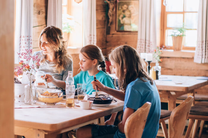 Eine Mutter sitzt mit ihren zwei Töchtern in einer Hütte am Tisch und alle zusammen essen