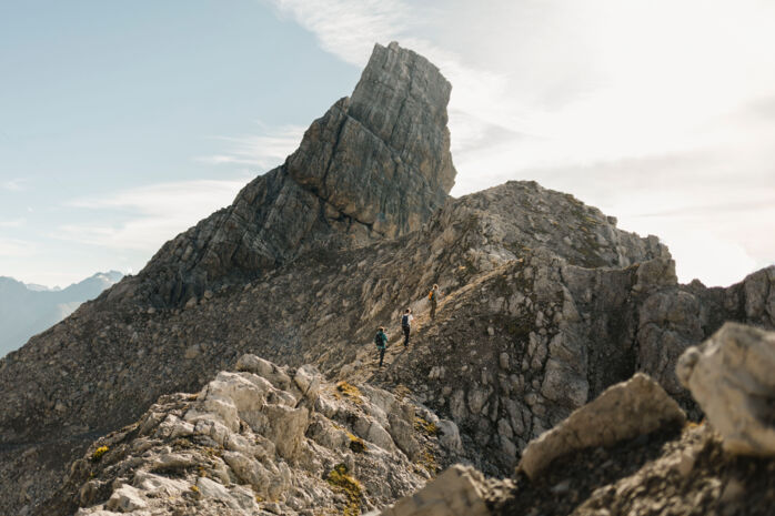 Drei Wanderer gehen in der Ferne an einem felsigen Gebirgsgrat