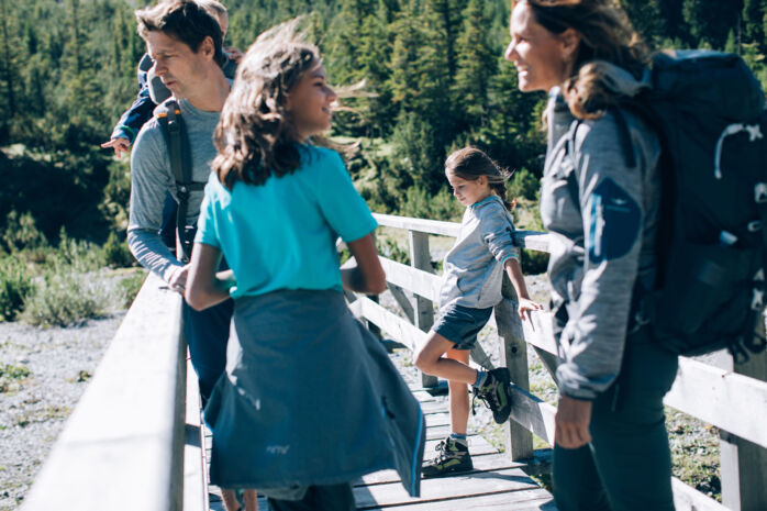 Eine Familie mit zwei Kinder in Wanderbekleidung macht Pause auf einer Bruecke die ueber den Lech fuehrt