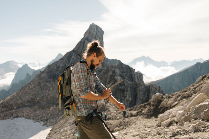 Wanderer steht am felsigen Grat und im Hintergrund ist ein weitläufiges Gebirgspanorama zu sehen