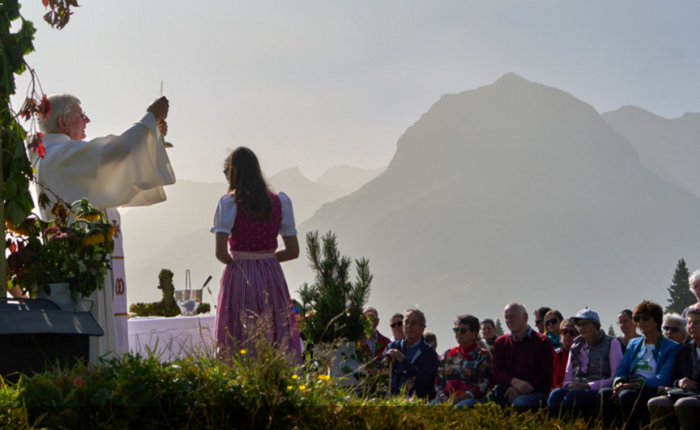 Ein Pater hÃ¤lt eine Messe vor einem Bergpanorama