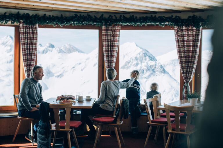 einige Personen genießen die Kulinarik und die winterliche Aussicht in Lech in Vorarlberg beim Einkehren