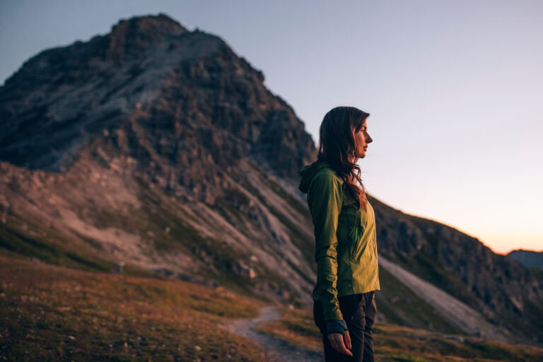 Wanderin steht am Berg in der Morgensonne und blickt in die Ferne