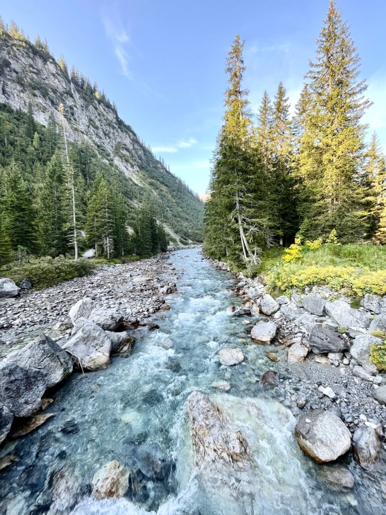 Blick auf den Lech wie er zwischen grünen Bergwiesen sein steiniges Flussbett zieht