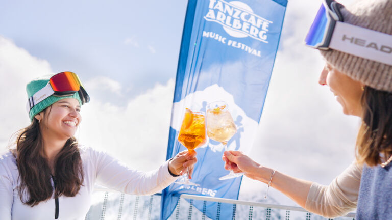 zwei Skifahrerinnen stoßen beim Tanzcafe Arlberg miteinander an 