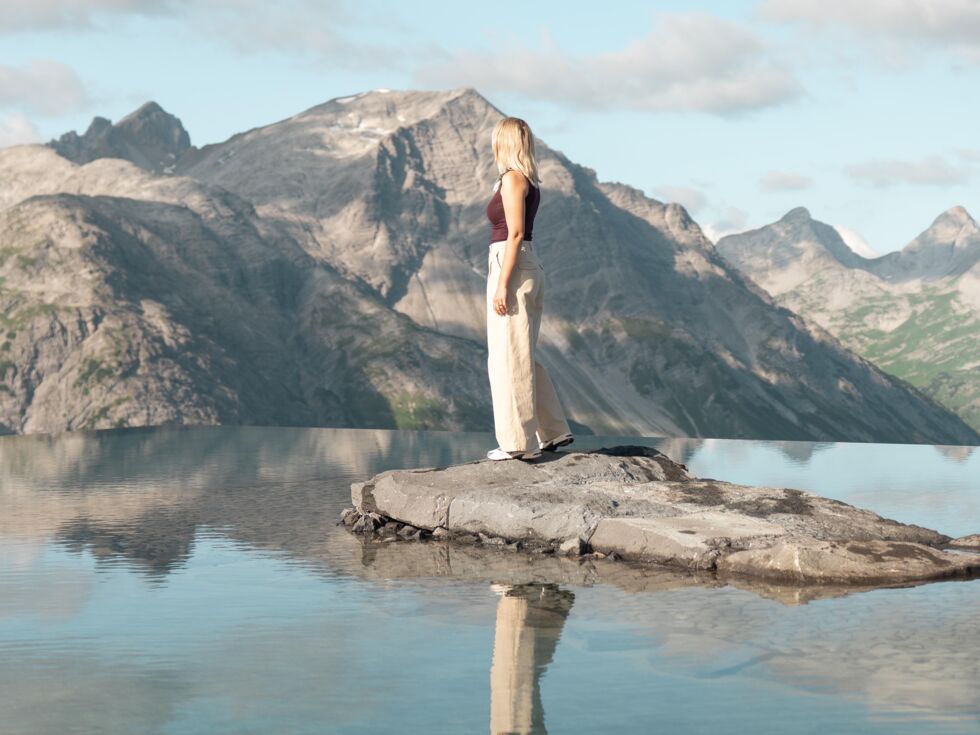Frau auf Felsen in einem spiegelnden Bergsee vor schroffem Alpenpanorama.